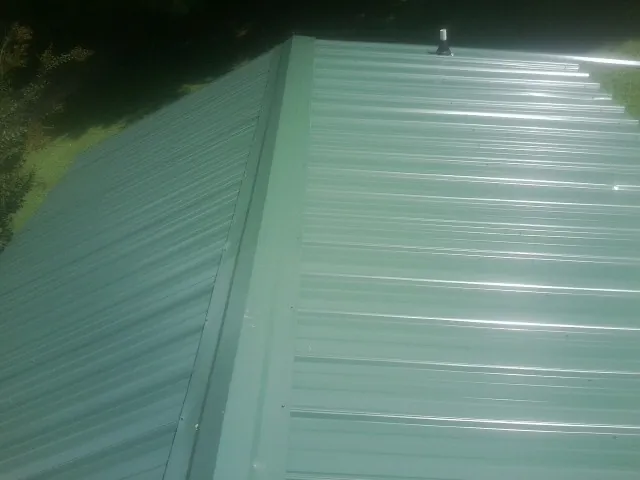 New green metal panels meeting at the ridge of a roof — Flat Roof Repair work by our crew in Loretto