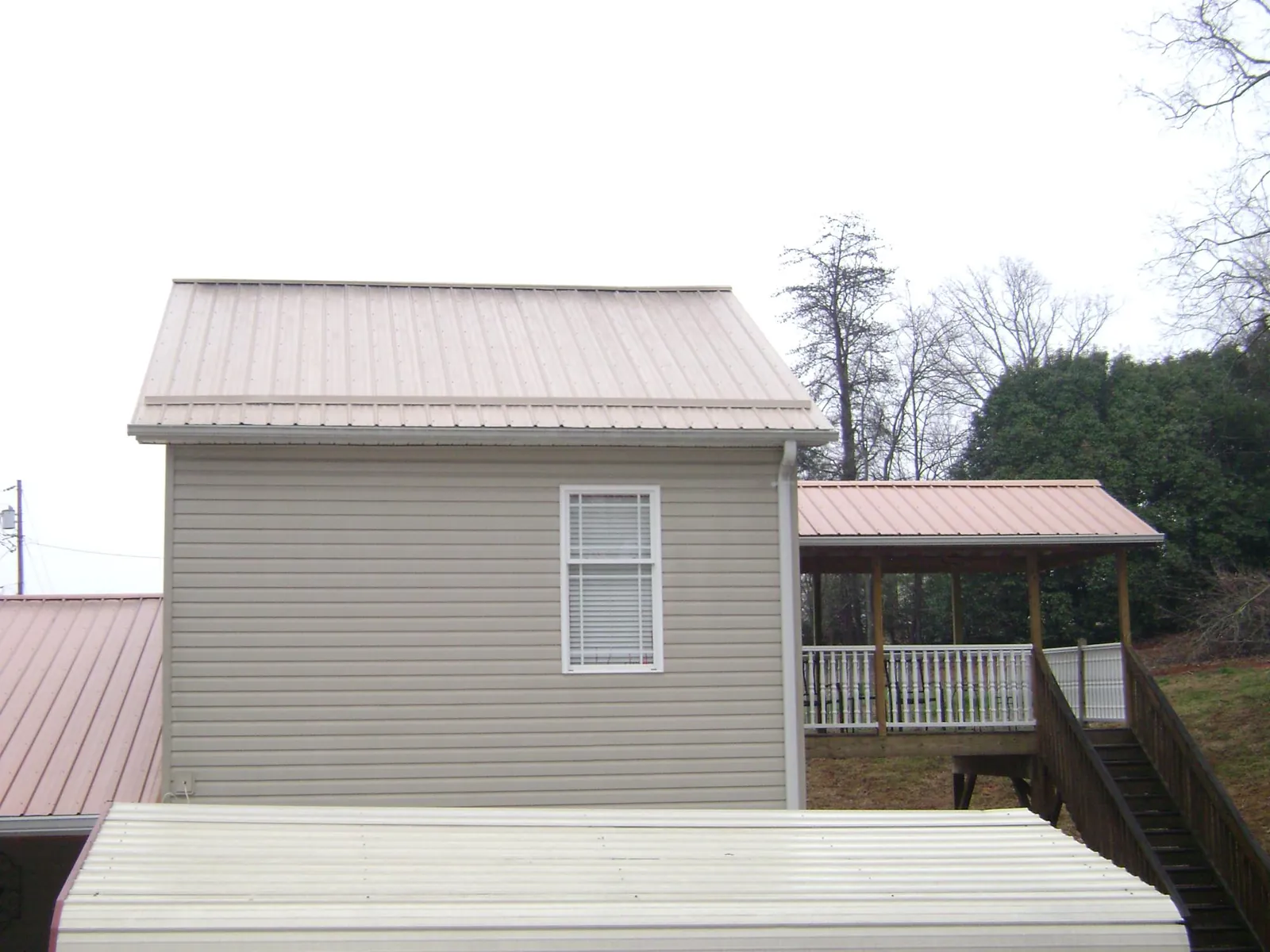 Tan metal roofs on a two story addition and attached porch, from a Roof Replacement job in Loretto